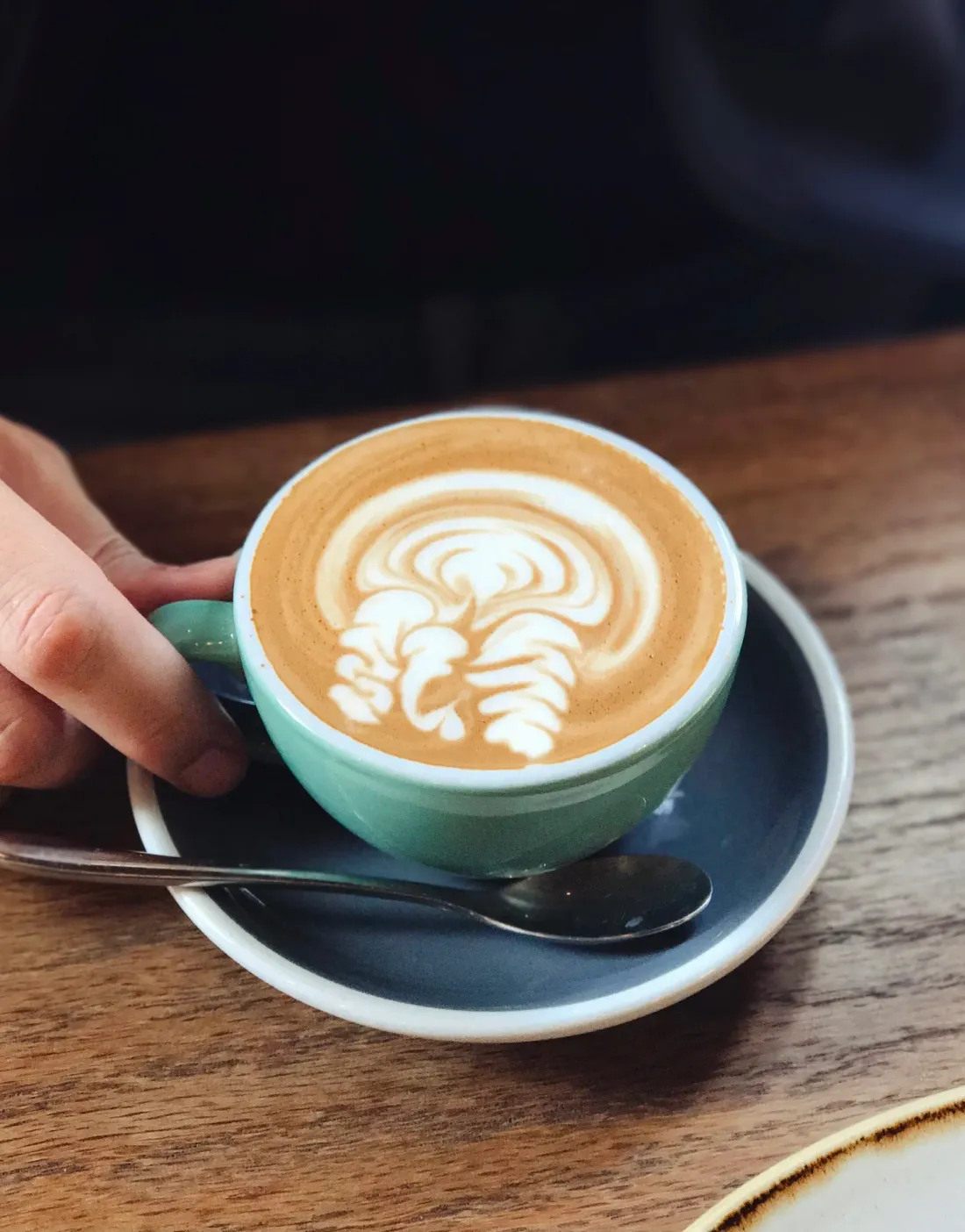 A flat white with latte art in a sage-green cup — specialty coffee at Cookie Beacon