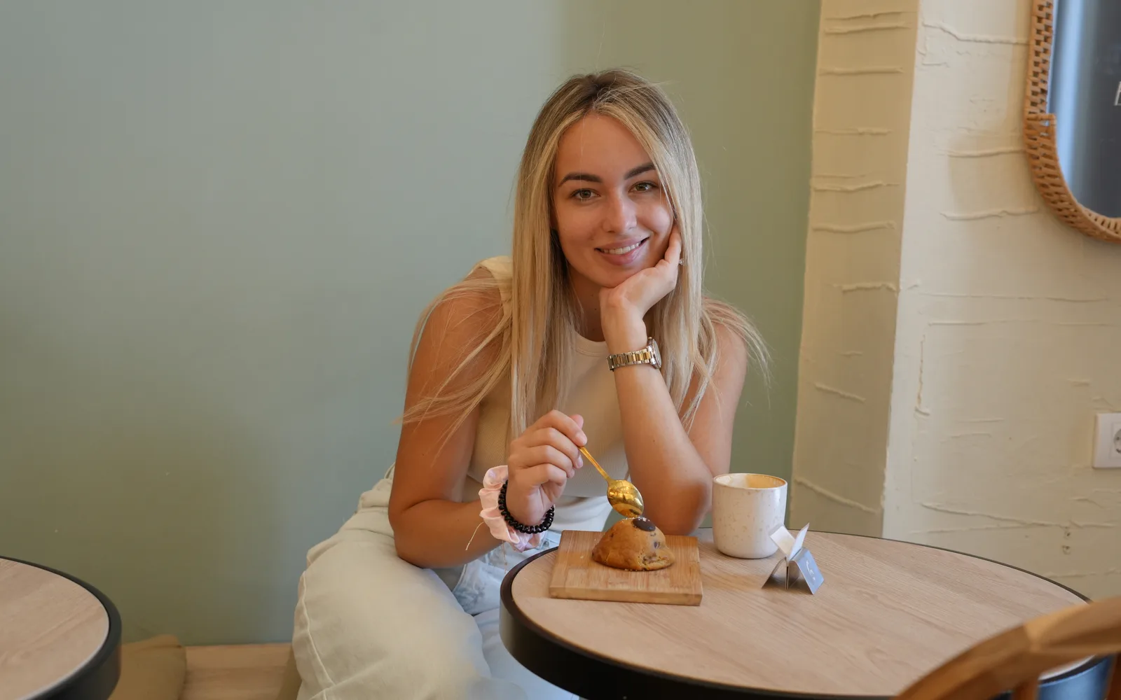 Gost za okruglim drvenim stolom u Cookie Beacon-u na Kralja Petra u Beogradu, sa kašikom iznad chunky kolačića na dasci i cappuccinom pored zida boje žalfije