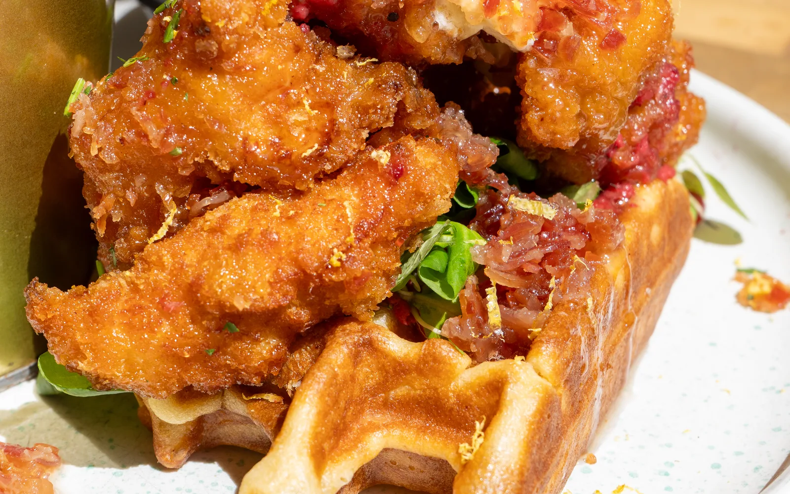 Close-up of the Chicken & Waffles Stack at Cookie Beacon Budapest — panko-crusted chicken over lamb's lettuce and a crimson smear of beetroot hummus, on a golden waffle glazed with smoked bacon sauce