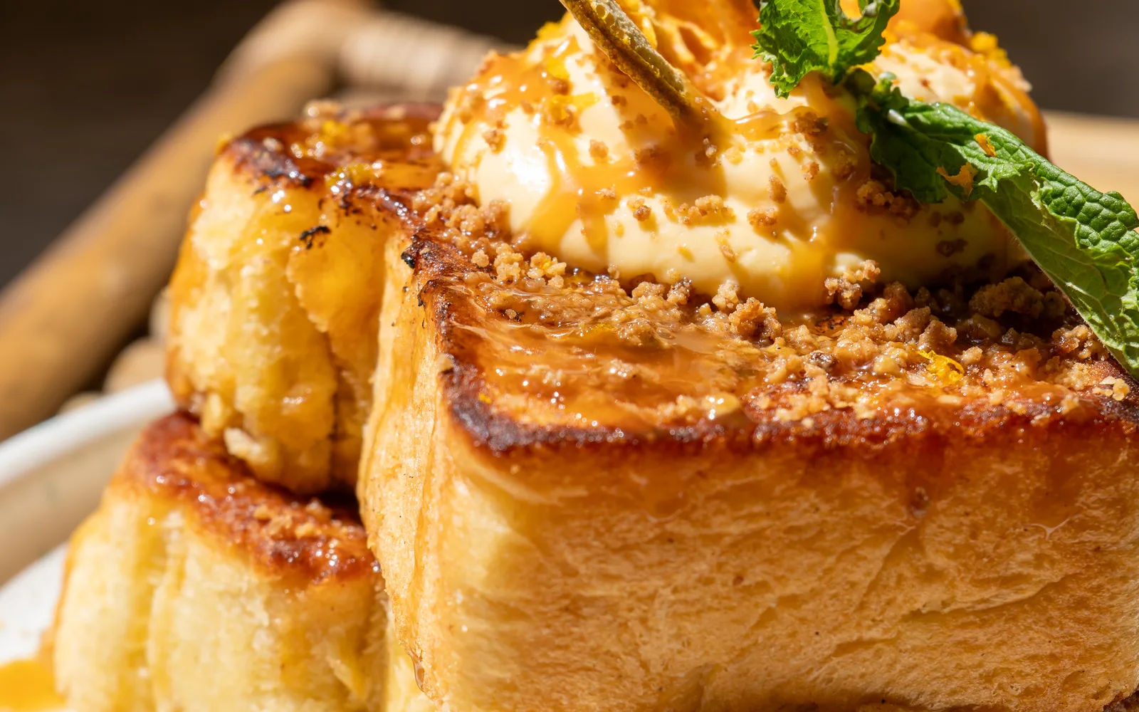Close-up of the Crème Brûlée French Toast at Cookie Beacon Budapest: orange pastry cream on a thick slice of brioche, scattered with cinnamon crumble and drizzled with salted caramel, with a sprig of mint and the edge of a dried orange slice