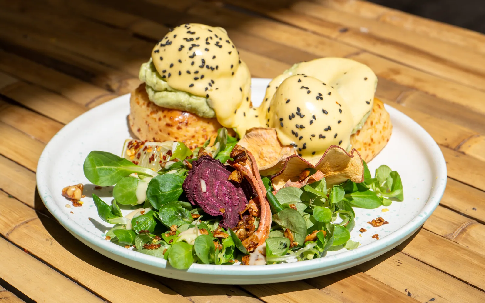 Eggs Benedict on cheddar scones at Cookie Beacon Budapest — two poached eggs under hollandaise on golden cheese-flecked scones, with smashed avocado and leafy greens