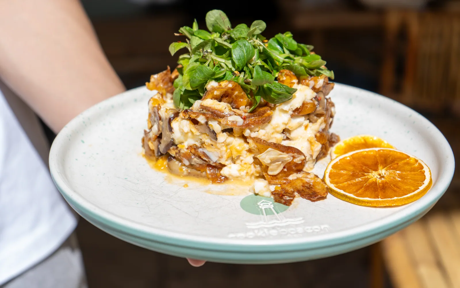 A plate of Madrid Smashed Eggs carried to a table at Cookie Beacon, the potatoes and shiitake folded through the egg