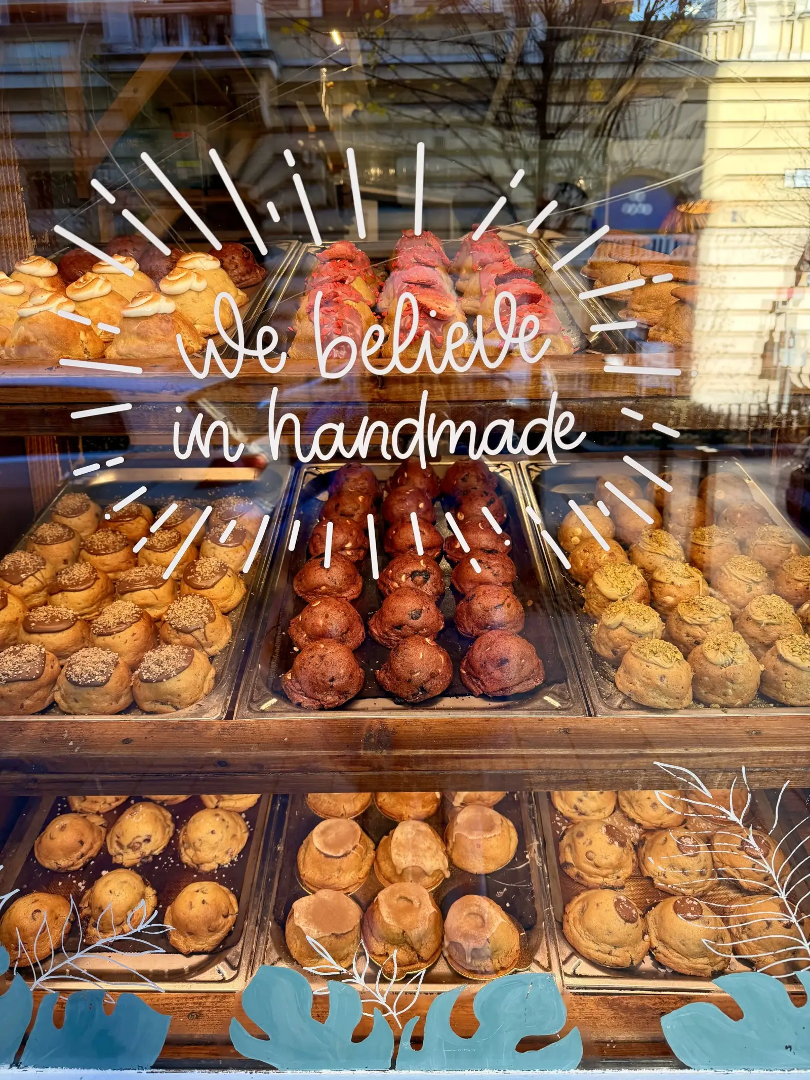 A Cookie Beacon brunch spot window filled with handmade cookies and pastries under a hand-lettered ‘we believe in handmade’ sign
