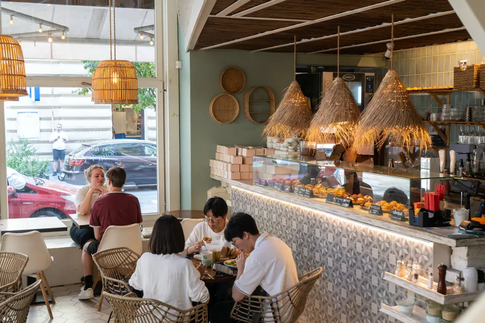 Two guests sharing a brunch plate at a table at Cookie Beacon Budapest, with the counter and a bowl of oranges behind