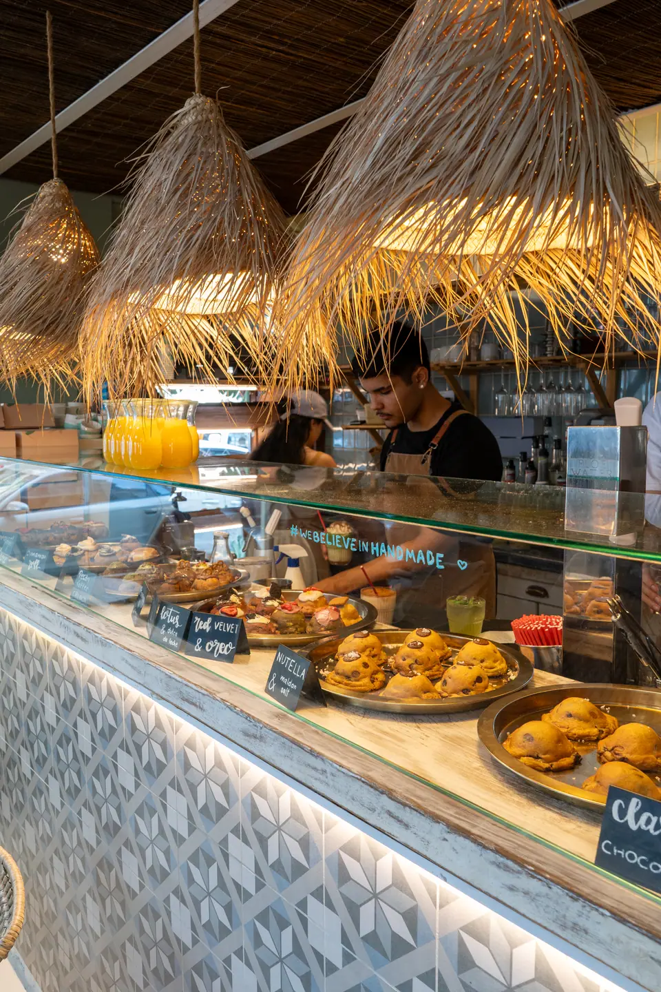 The pastry counter at Cookie Beacon Budapest with plates of chunky cookies, chalk price labels and a baker working behind it