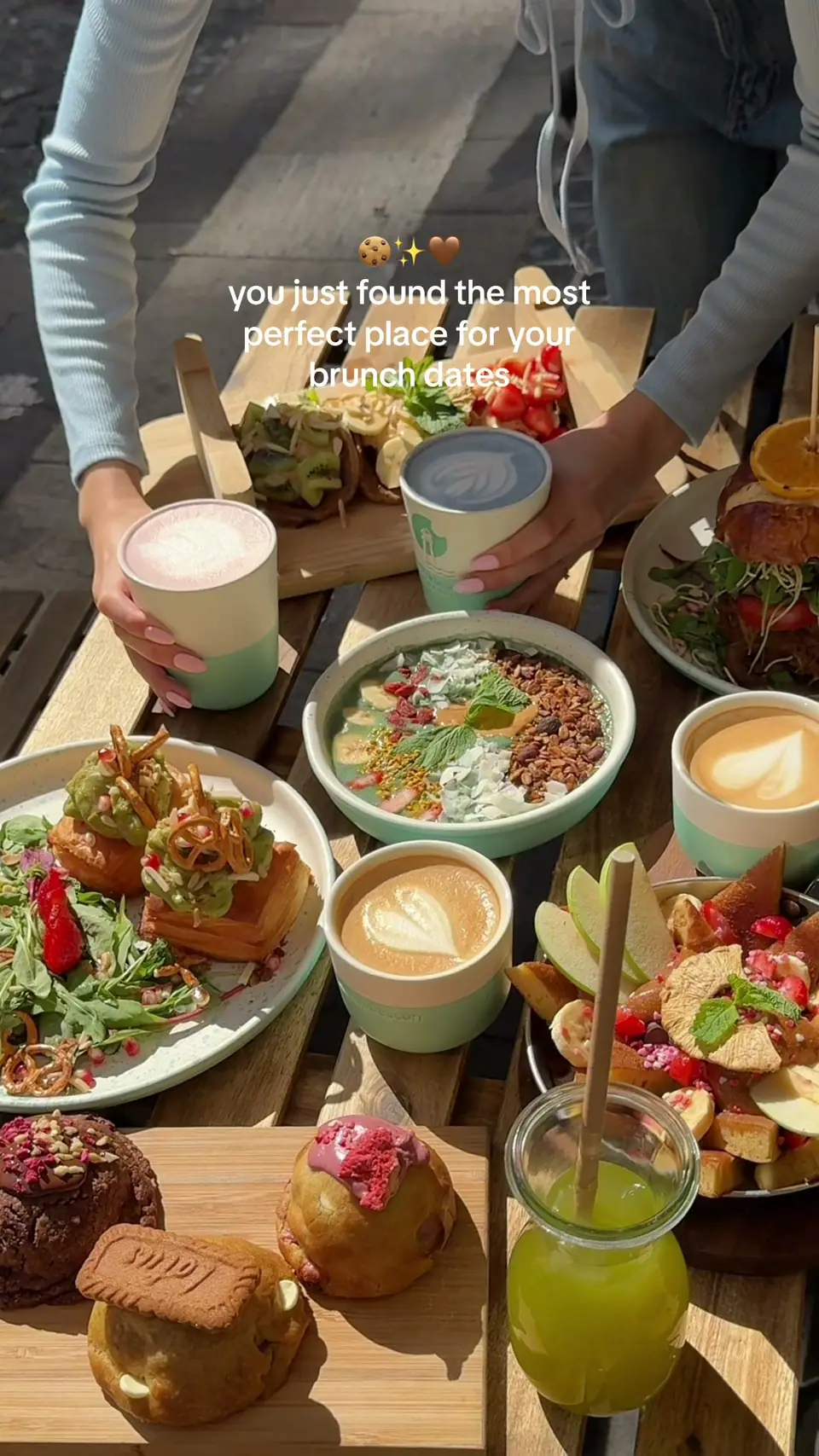 Overhead view of a full brunch table outside Cookie Beacon Basilica on Hercegprímás utca — avocado toast, a yoghurt and granola bowl, two lattes with latte art, a green juice, pastries and a chunky cookie
