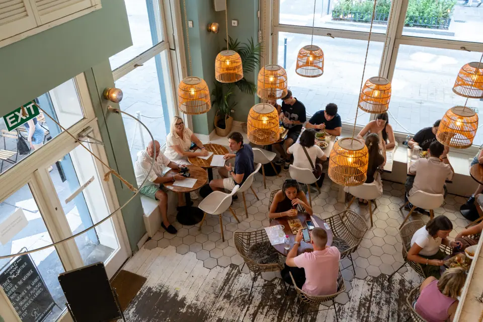 Looking down from the mezzanine at Cookie Beacon Budapest onto guests at hexagon-tiled tables under glowing rattan lamps