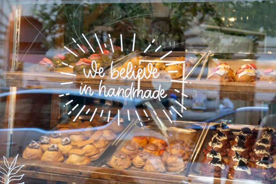"We believe in handmade" hand-lettered on the window of Cookie Beacon Budapest, with trays of chunky cookies behind the glass