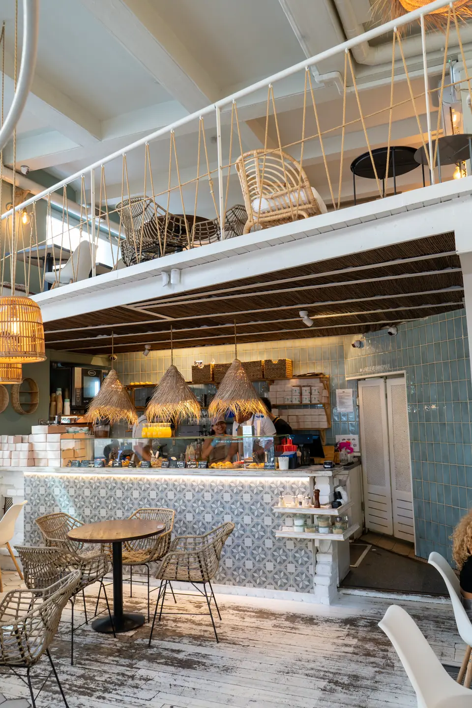 The white mezzanine structure above the tiled counter at Cookie Beacon Budapest, stacked rattan chairs on the deck