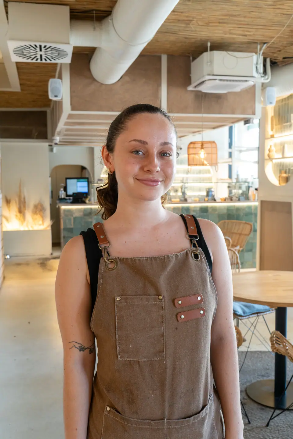 A Cookie Beacon staff member in a brown canvas apron standing in front of the green-tiled counter and the till at the Ferenciek tere café